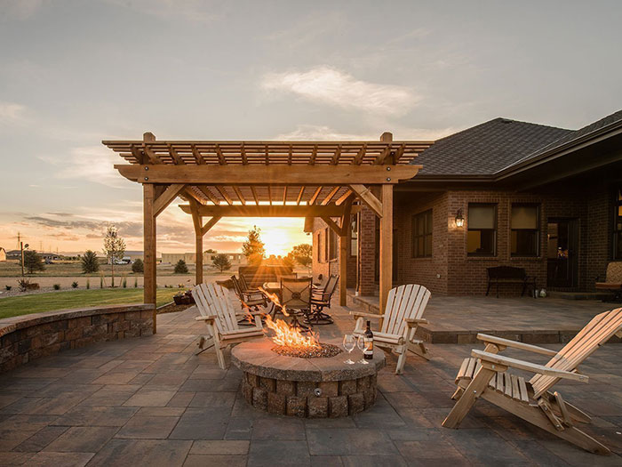 a concrete fire pit surrounded by wooden chairs and a pergola at the back